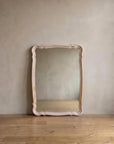 Blush French Provincial style mirror leaning against a greige plaster wall on a reclaimed wood floor