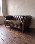 Three-quarter view of the tufted leather chesterfield loveseat with brass nailhead scroll arm