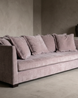 Alternate three-quarter view of the sofa against bare plaster with stoneware vessels and dried branches