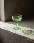 Gold-Rim Swirl Coupe, uranium glass, bare on a greige plaster ledge