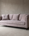 Long low dusty rose chenille sofa with slim vertical panel arms and a single bench cushion, in a greige troweled plaster room