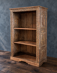 Carved wooden bookcase, bare, with paneled side and aged brown and pale finish.