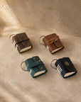 Four miniature leather journal keyrings in brown elastic, brown strap, teal and blue button, on travertine