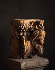 Antique carved teak temple capital from India, parrot brackets and beaded garlands, displayed on a stone plinth in dramatic light