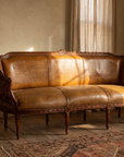 The Marea Settee, carved walnut frame and burnished cognac leather, styled in a warm room