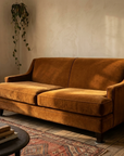 Cognac velvet mid-century sofa, three-quarter view showing tapered steel-capped legs