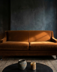 Cognac velvet sofa centered against smoke-stained dark plaster walls with candles