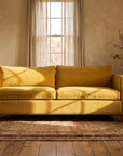 Mustard velvet mid-century sofa, front view in a warm plaster room