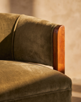 Macro detail of olive velvet pile, piped seam and polished cherry wood arm cap