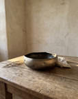 Dimpled metal bowl on an aged oak table in a warm plaster room corner