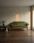 Green velvet sofa styled with antique wooden side table and dark ceramic vessel