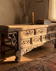 Side three-quarter view of the antique elm altar table with warm sun across the carved apron