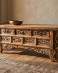 Front three-quarter view of the carved elm altar table in a warm plaster room