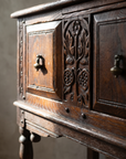 Detail of the carved floral relief stile, brass teardrop pulls, and turned leg