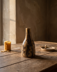 Tall narrow-necked stoneware bottle vase painted with climbing branches and leaves, on a weathered oak table