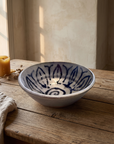 Shallow pale stoneware bowl with a deep indigo lotus painted inside, on a weathered oak table