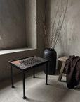 Antique Grate Side Table, Floral Scroll design, styled in a greige plaster room with a stoneware vessel and dried branches