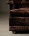 Front corner detail showing the rolled arm cap, welted seat cushion edge, plinth base band and original front caster