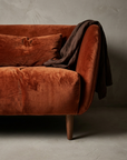 Front corner of the sofa with chocolate linen draped over the arm and the rounded apron rolling into the walnut leg