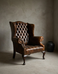 Three-quarter view of the button-tufted leather wingback chair with rolled scroll arms and cabriole legs