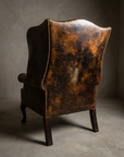 Rear view of the wingback chair showing the plain outside back leather with mottled patina and brass nailhead trim