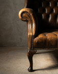 Detail of the rolled arm scroll with antique brass nailheads following the spiral, cabriole leg below