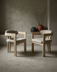 Pair of sueded white Pigreco-style armchairs in pale ash, angled toward each other in a greige plaster room with stoneware vessels and dried branches