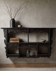 Antique carved black wall shelf styled as a curated display shelf with books, ceramics, and dried branches