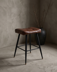 Three-quarter view of the pleather saddle counter stool showing the tufted seat and tapered legs
