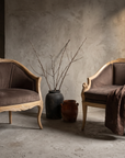 Both carved whitewashed bergere chairs together in a plaster room, wheat motif and dog head motif