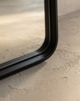 Macro detail of the mirror's bottom corner showing the matte black frame profile and rounded join