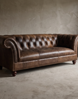The Umber Chesterfield, three-quarter view showing tufted back, rolled arms, and nailhead trim, matte worn leather