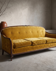 Vintage carved-wood camelback sofa in gold velvet against raw plaster wall