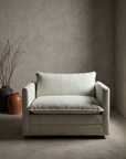 Chair and a half in white, lifestyle shot in a greige plaster room with stoneware vessels