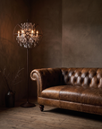 Crystal Orb floor lamp in a dim, sultry living room corner beside The Umber Chesterfield sofa, warm amber glow