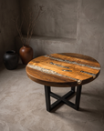 Creeklight Parlor Table, round hardwood and crushed glass river coffee table on a matte black steel X-frame base, in a greige plaster room