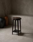 Rustic accent stool with worn dark paint on octagonal top, styled with stoneware vessels and dried branches in a plaster room
