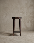 Straight-on front view of the rustic accent stool showing its full silhouette against a plaster wall