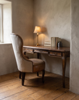 The Cabriole Writing Desk paired with a leather and linen wingback chair in a cozy plaster nook with warm lamp light