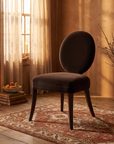 Mitchell Gold + Bob Williams oval-back dining chair in espresso brown velvet, three-quarter view, warm candlelit room