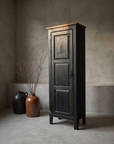 Little Pantry Armoire, narrow black distressed pantry cabinet, lifestyle hero in a greige plaster room with stoneware vessels and dried branches