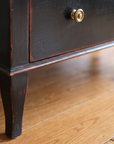 Detail of the tapered leg, worn ebonized finish, and brass ring pull