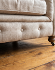 Low detail of the tufted base rail with its single row of buttons, a turned wood leg and brass caster on the reclaimed wood floor