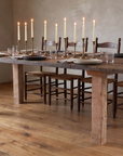 Redwood dining table set for an evening dinner with lit taper candles in brass candlesticks, stoneware plates and clear water glasses