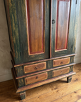 Close detail of the armoire's four-drawer base with red-brown drawer panels, iron ring pulls, and block feet