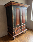 Three-quarter view of the Batavia Armoire showing its stepped ochre and red cornice and side depth