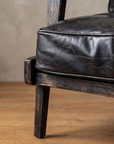 Close-up of the black top-grain leather seat cushion with piping and distressed black oak leg