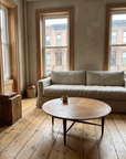 The Aurelia round mid-century walnut coffee table in a prewar Harlem apartment with plaster walls, a linen sofa, and wide plank floors