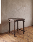 Three-quarter view of the vintage Indian side table alone, showing the plank top, metal corner plates and leg stretchers