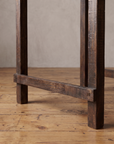 Detail of the square legs and low stretcher in dark reclaimed wood on a wide-plank floor